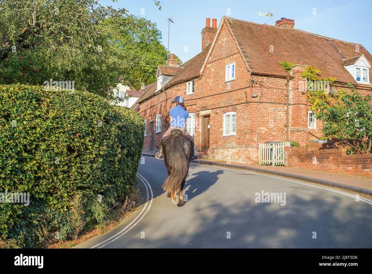 Vue arrière d'un homme à cheval sur une route étroite à travers un village typique de campagne anglaise sous le soleil d'automne. Banque D'Images