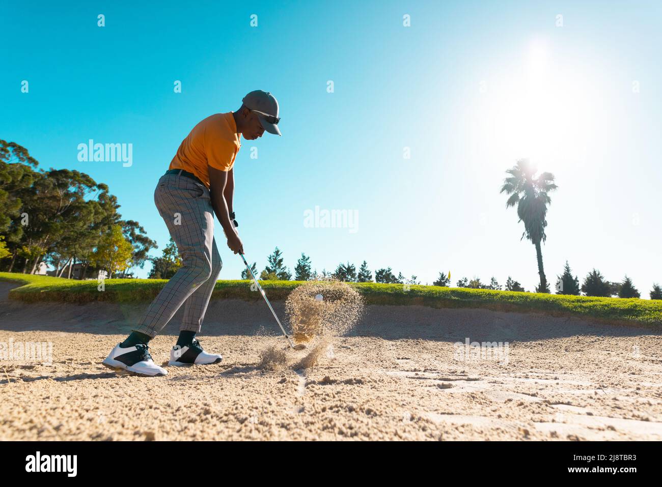 Vue latérale d'un jeune homme afro-américain qui frappe avec un club de  golf sur le sable contre un ciel dégagé sur le parcours Photo Stock - Alamy