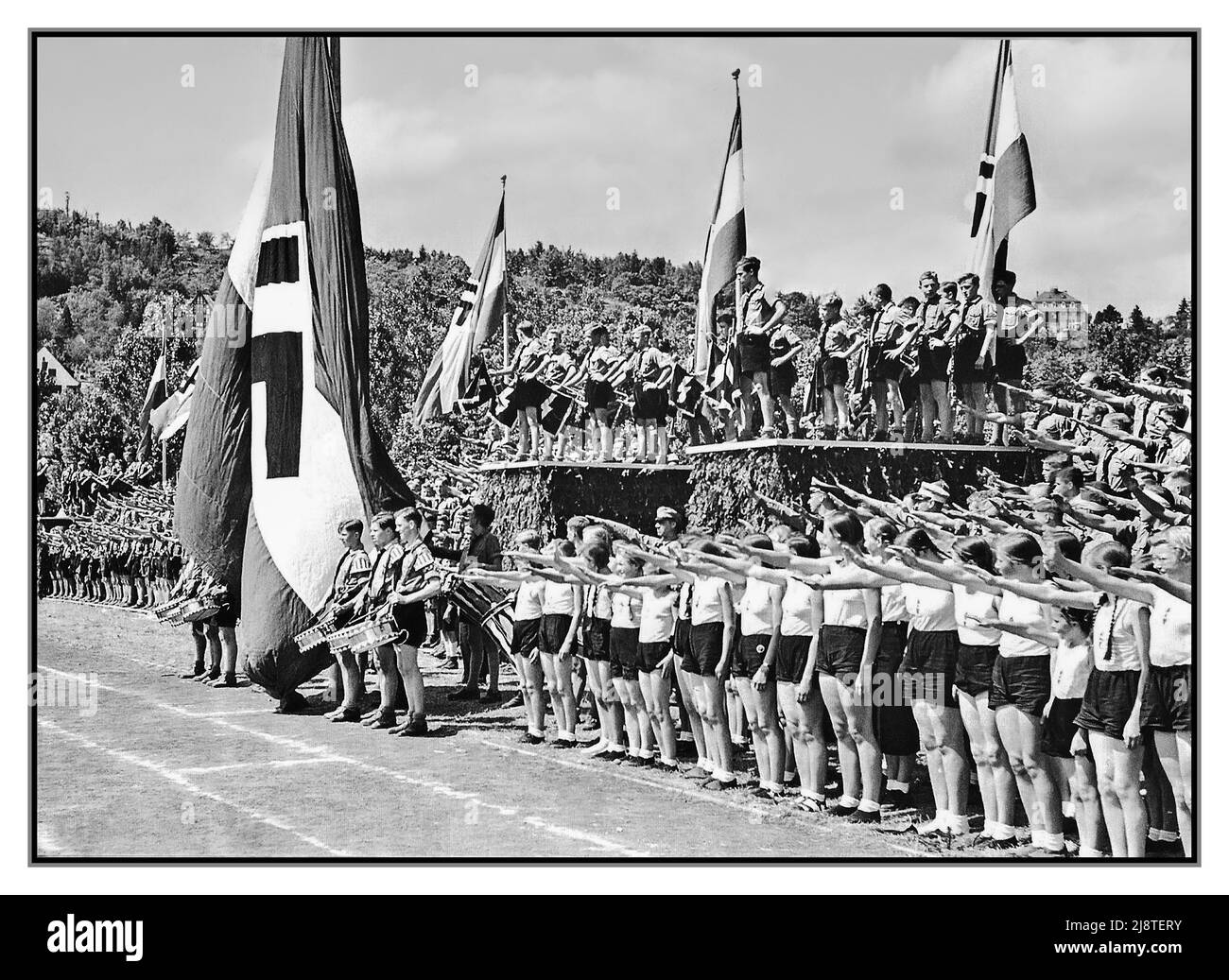 1930s Hitlerjugend Hitler Jeunesse avec BDM la Ligue des filles allemandes ou la bande des Maidens allemands Bund Deutscher Mädel, abrégé en BDM l'aile des filles du mouvement de jeunesse du Parti nazi de la Jeunesse Hitler. C'était la seule organisation légale de jeunesse féminine en Allemagne nazie. Ensemble lors d'un festival sportif régional de la Jeunesse Hitler et du BDM à Tübingen sur le terrain sportif universitaire avec des drapeaux et des bannières Swastika donnant le salut nazi Tubingen Allemagne nazie 1937 Banque D'Images