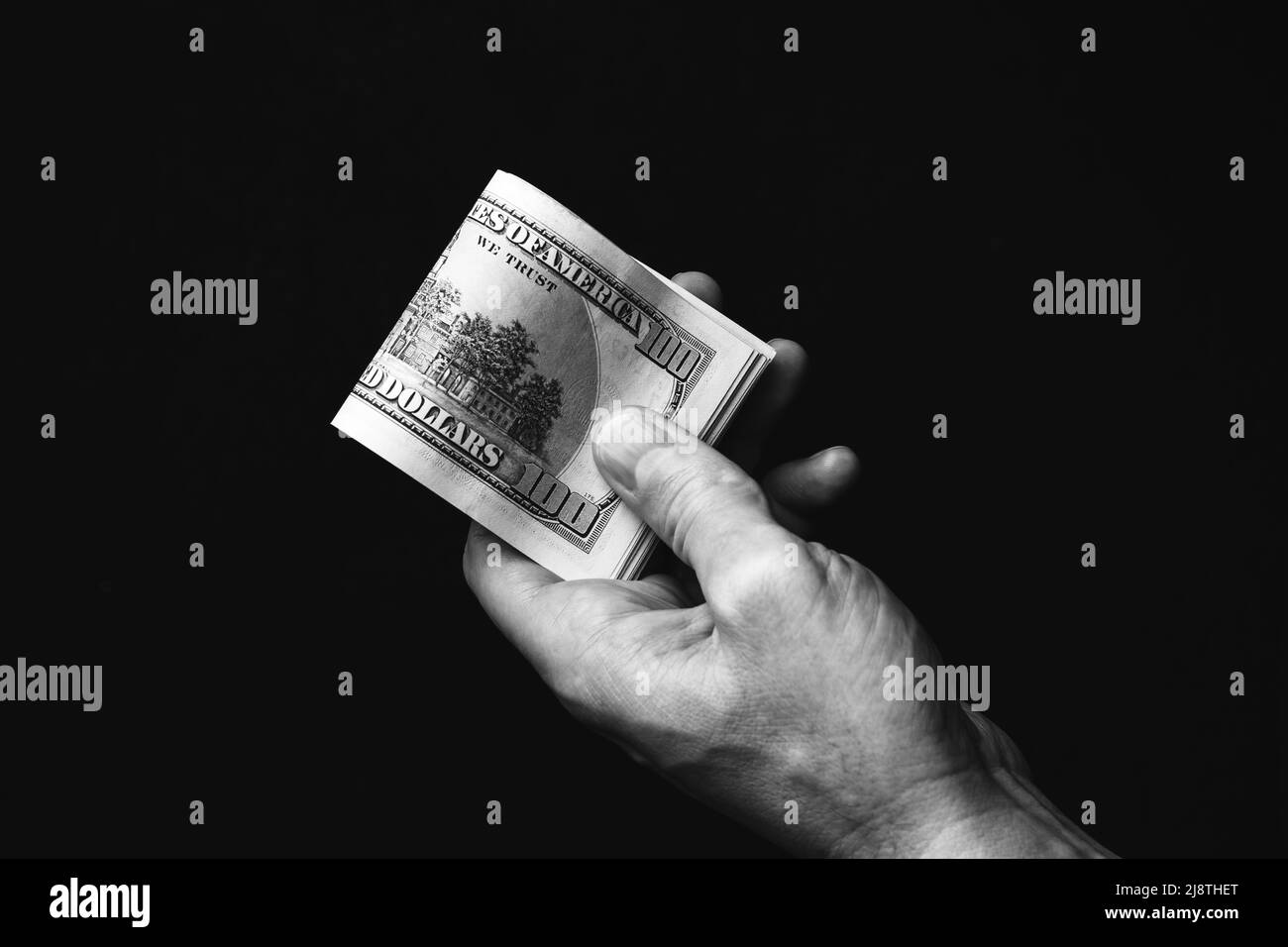 Main masculine nous tenant des billets de cent dollars sur fond noir. Un homme avec de l'argent américain en gros plan. Photo en noir et blanc Banque D'Images