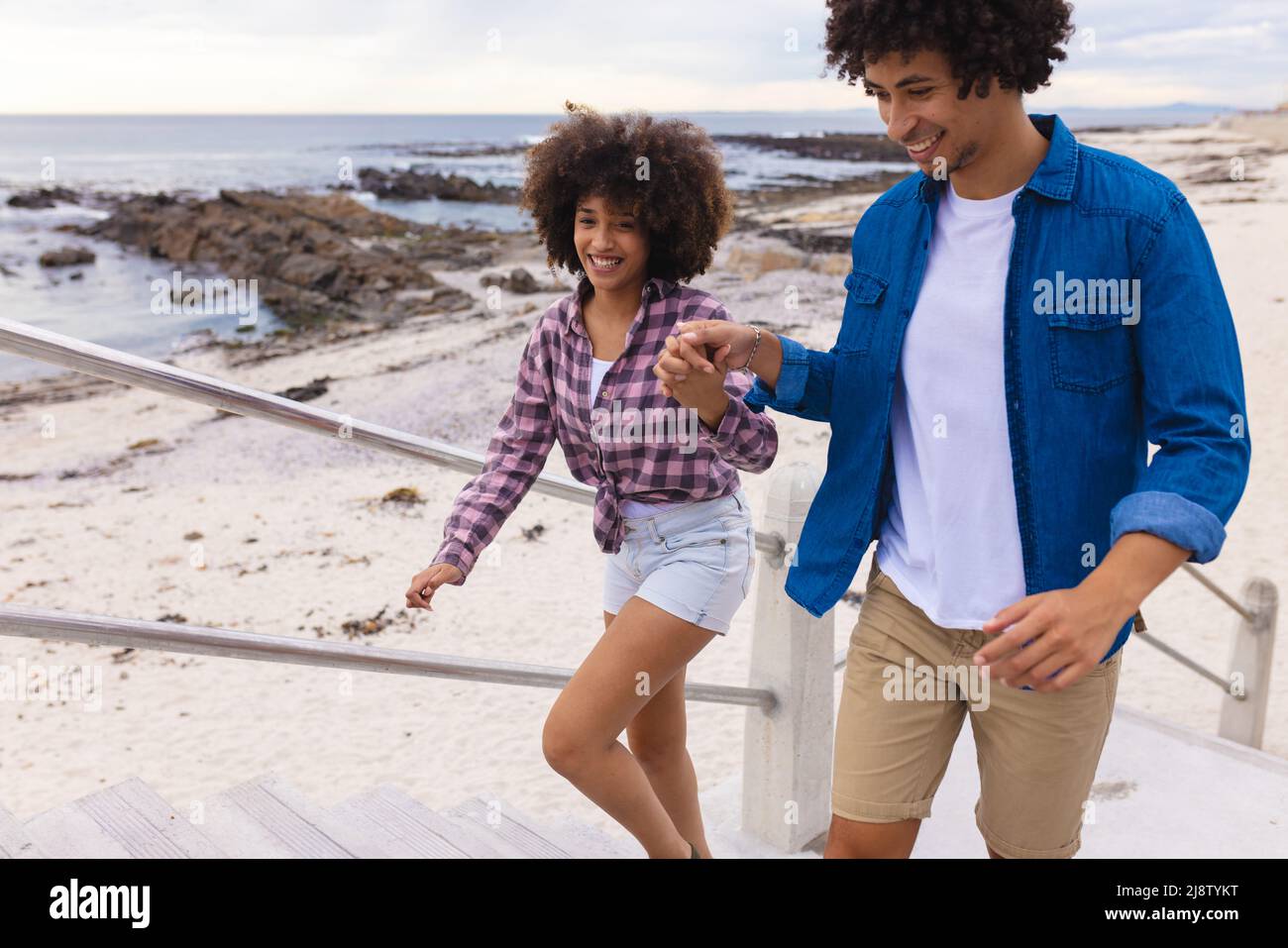 Jeune couple afro-américain souriant tenant les mains tout en grimpant sur les marches de la plage Banque D'Images