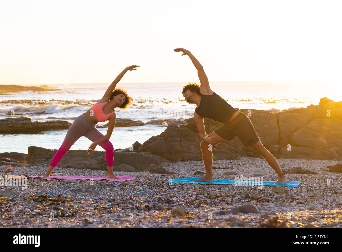 Un jeune couple afro-américain se penche sur le côté tout en faisant du yoga à la plage pendant le coucher du soleil, espace de copie Banque D'Images