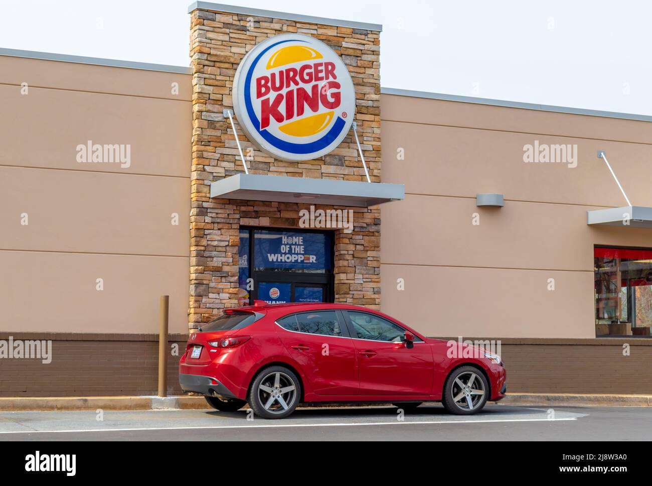 Extérieur, enseigne de la marque et logo « Burger King » à la fenêtre du drive-in, sous la lumière du petit matin, par beau temps ensoleillé, avec un véhicule rouge. Banque D'Images