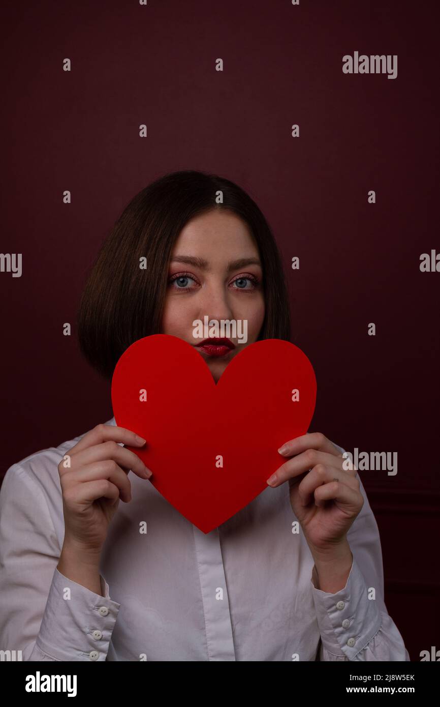 Femme à poils courts sur fond rouge tenant le cœur rouge devant son menton Banque D'Images