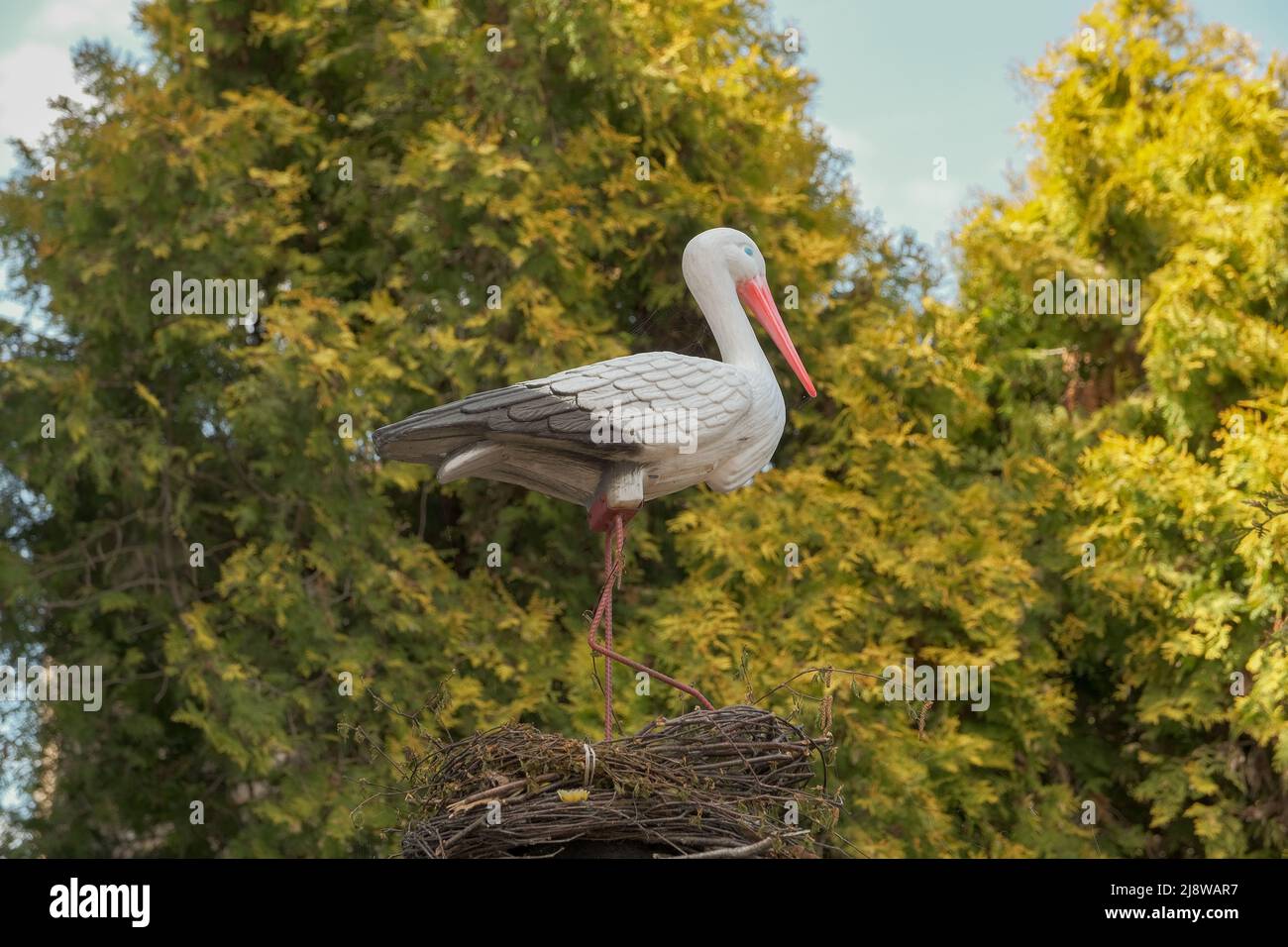 Cigogne artificielle dans le jardin. Statues de cigognes. Cigogne d'oiseau en plastique dans l'herbe. Élément de décoration . cigogne artificielle dans le nid . Banque D'Images