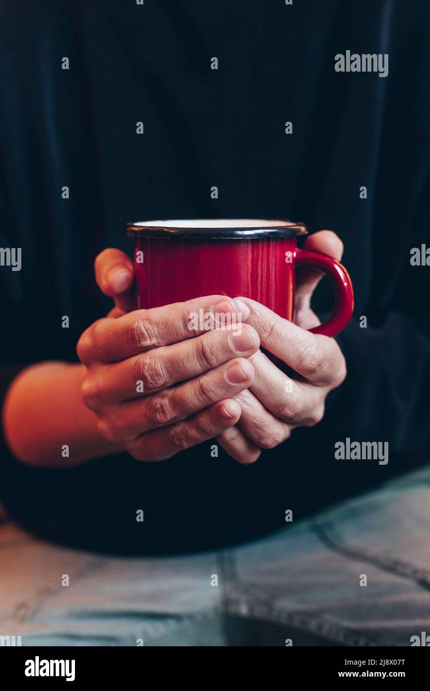 Gros plan des mains d'une femme tenant une tasse rouge avec un fond sombre pour le contenu promotionnel, le café, le chocolat ou le thé. Banque D'Images