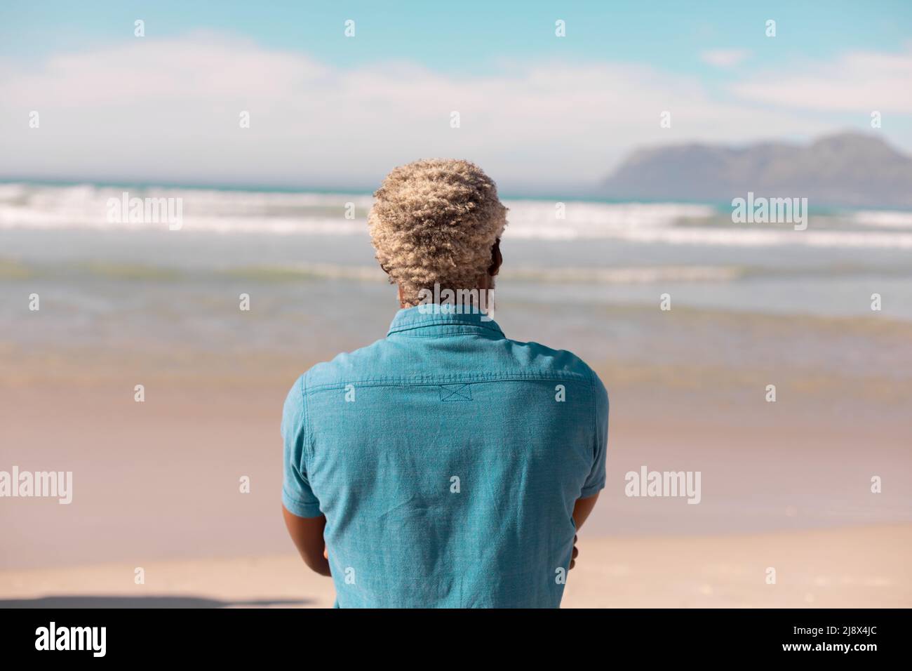 Vue arrière de l'homme senior afro-américain avec des cheveux gris regardant le paysage marin contre le ciel par temps ensoleillé Banque D'Images