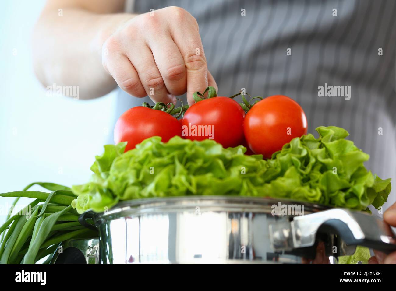 Le chef met les tomates mûres sur la laitue, l'homme prépare une nouvelle recette, essayez la nourriture végétarienne Banque D'Images