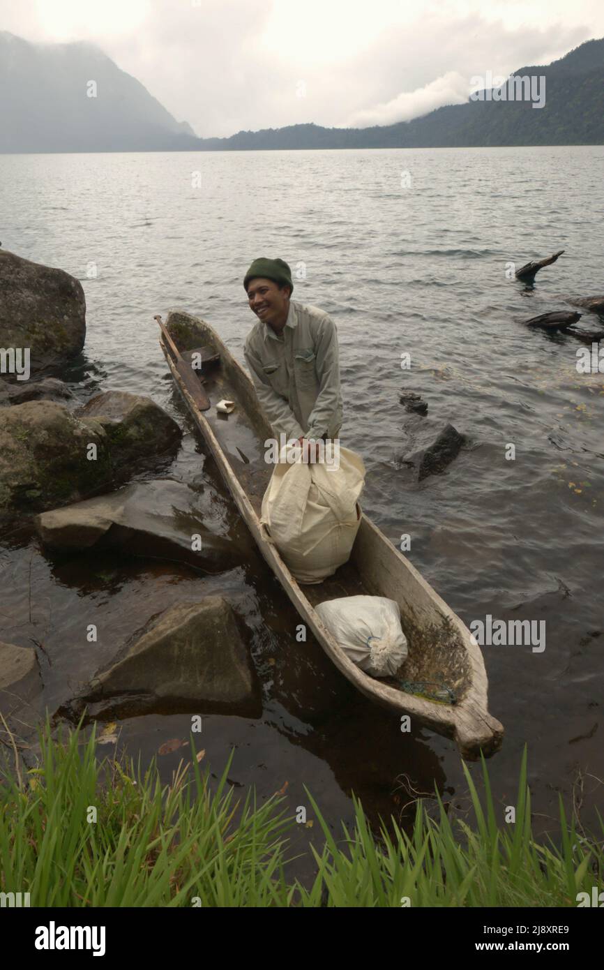 Une nourriture itinérante déchargeant un sac rempli de poissons d'eau douce fermentés de son bateau sur le lac Gunung Tujuh à Gunung Tujuh, Kerinci, Jambi, Indonésie. Banque D'Images