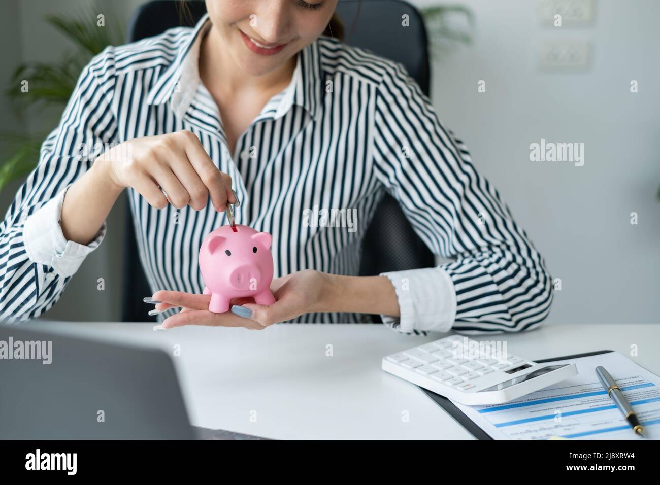 Portrait d'une femme d'affaires asiatique souriant mettant une pièce à l'intérieur de la piggy banque comme épargne pour l'investissement. Richesse et concept financier. Banque D'Images
