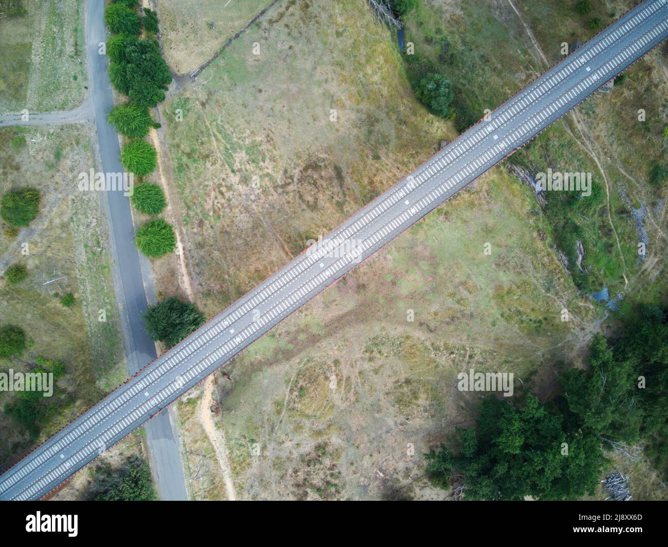 Voies ferrées vue aérienne montrant des lignes de chemin de fer parallèles, des arbres verts, des terres agricoles et des routes asphaltées dans la campagne australienne. Banque D'Images