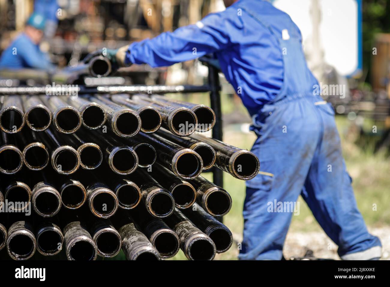 Tuyaux de forage de forage pétrolier empilés avec les travailleurs de l'industrie pétrolière en arrière-plan. Industrie du pétrole et du gaz. Cric de pompe de pétrole brut sur un champ de pétrole. Perçage d'huile et Banque D'Images