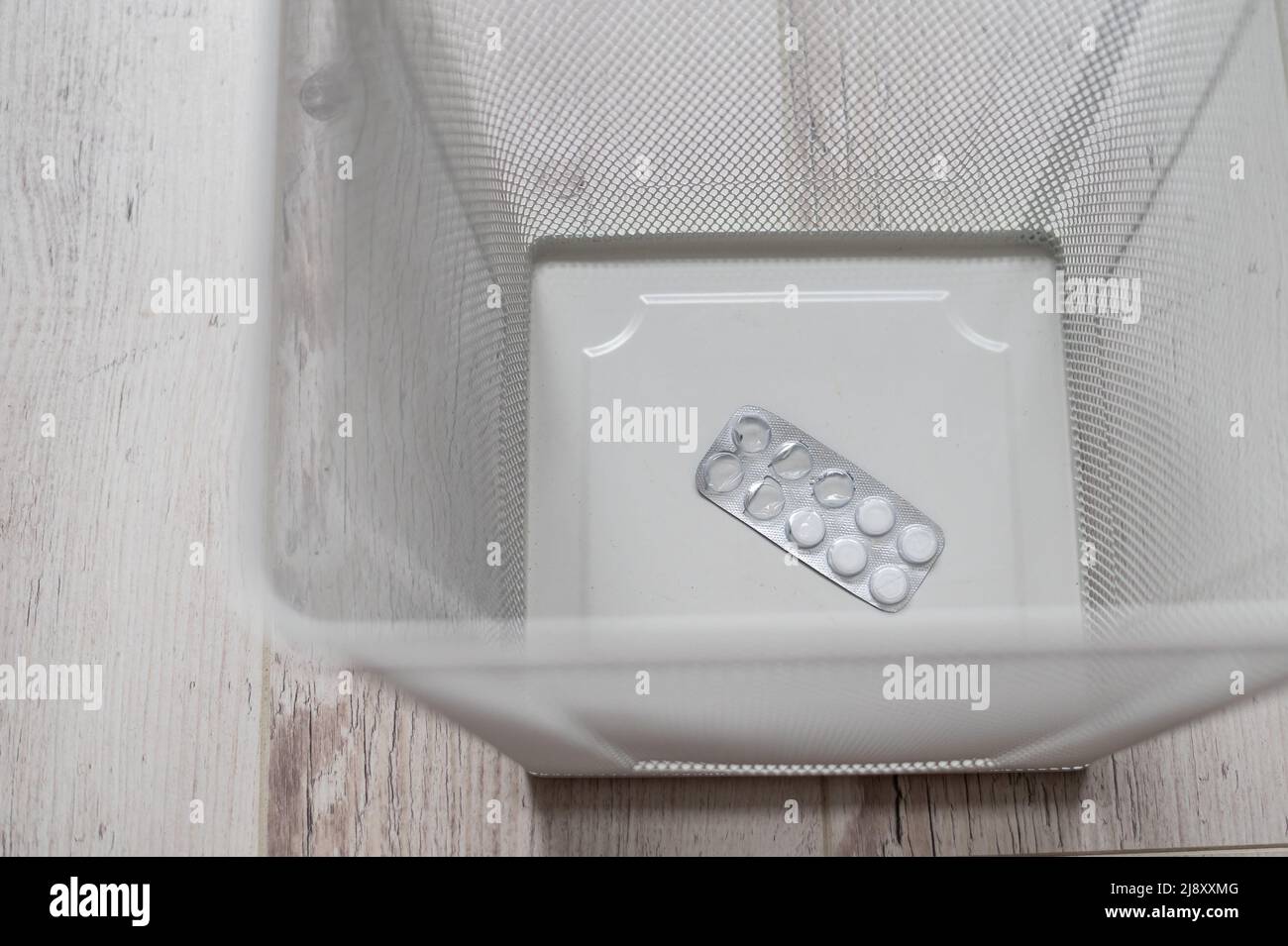 Médicament dans un panier à déchets en maille blanche. Une boursouflure de pilules jetées dans la poubelle. Un panier en papier avec des médicaments à l'intérieur sur un parquet. Banque D'Images