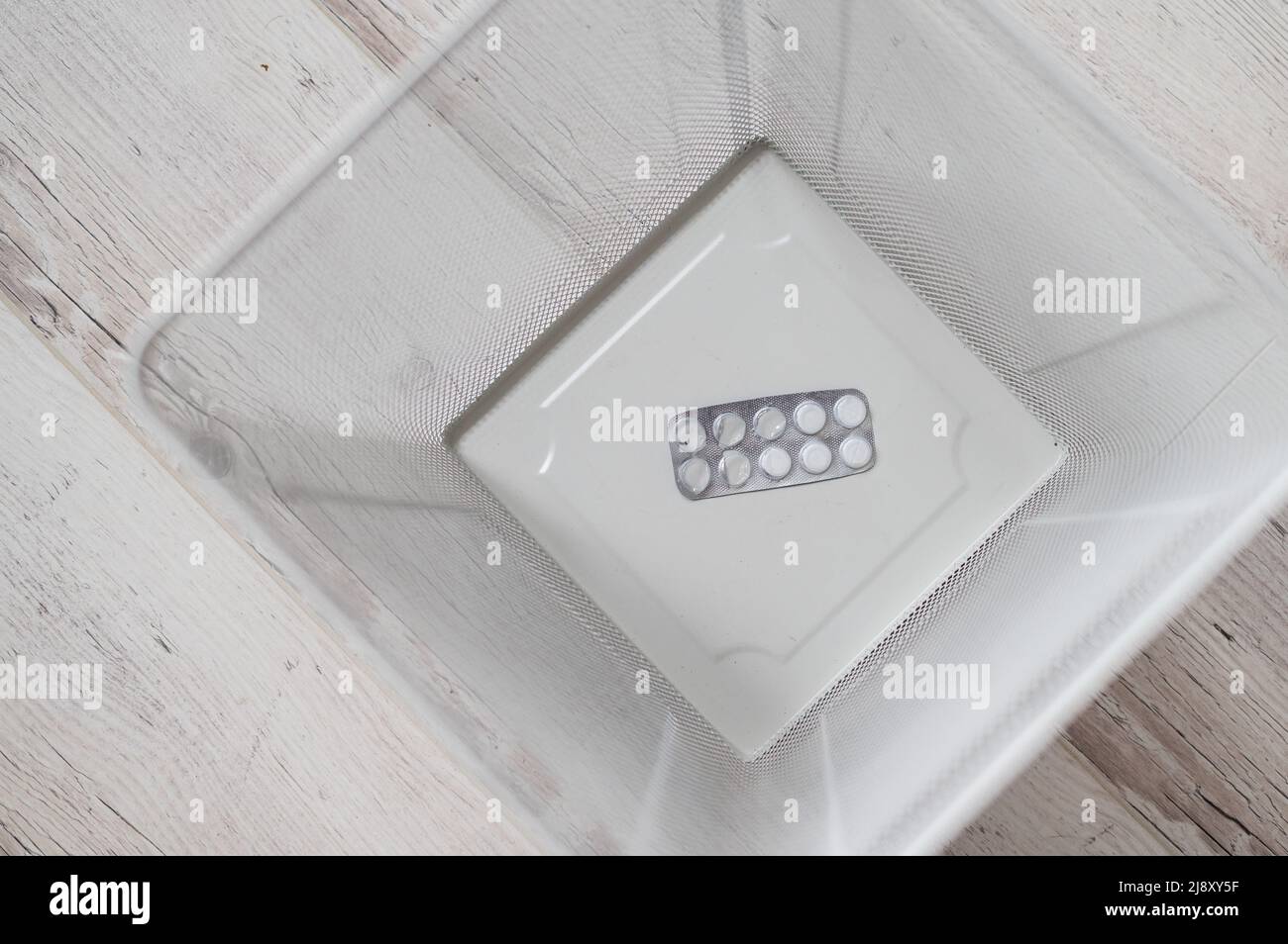 Médicament dans un panier à déchets en maille blanche. Une boursouflure de pilules jetées dans la poubelle. Un panier en papier avec des médicaments à l'intérieur sur un parquet. Banque D'Images