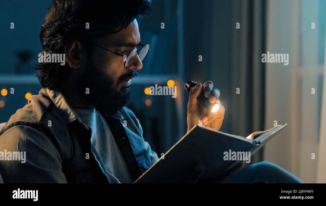 L'homme adulte barbu en lunettes la nuit, le salon avec lampe de poche brille sur le livre se prépare pour les examens de lecture de bible, concept de foi. 30s mec Banque D'Images