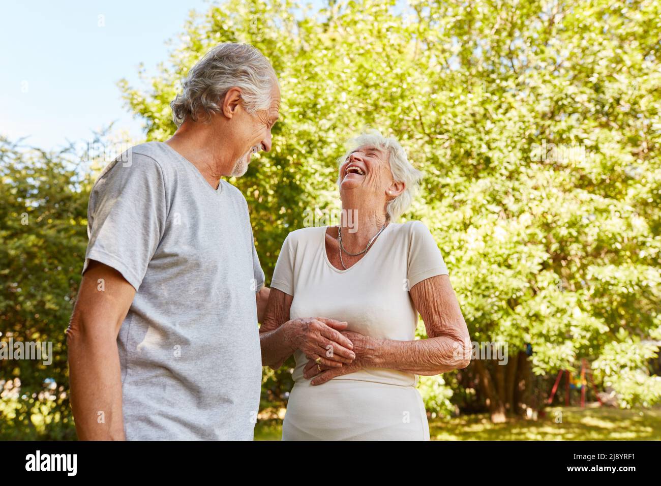 Couple heureux de personnes âgées dans la nature parlant et riant à haute voix avec leurs mains sur leurs estomacs Banque D'Images
