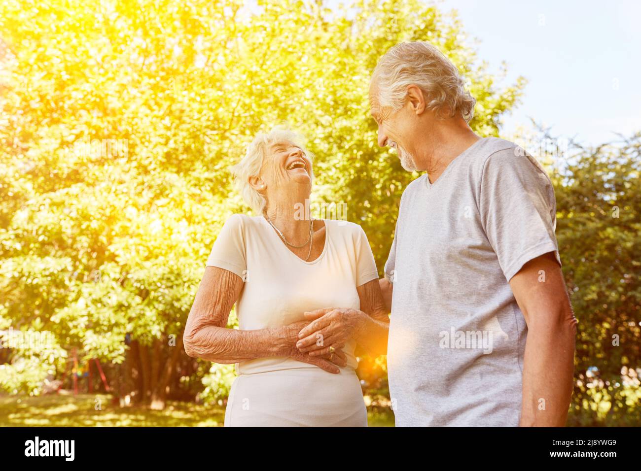 Couple heureux de personnes âgées riant ensemble à une blague dans la nature, tenant les mains sur les estomacs Banque D'Images