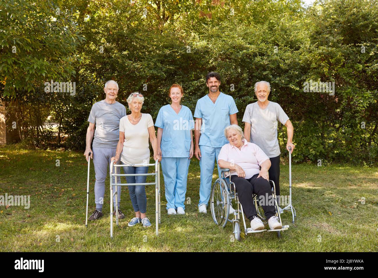 Groupe d'aînés avec fauteuils roulants et aides à la marche, ainsi que le personnel infirmier dans le jardin de la clinique de réadaptation Banque D'Images