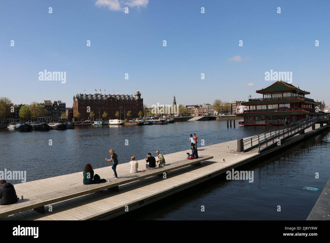 Touristes assis et marchant sur la jetée flottante sur le canal à Amsterdam près de la gare centrale, pays-Bas Banque D'Images