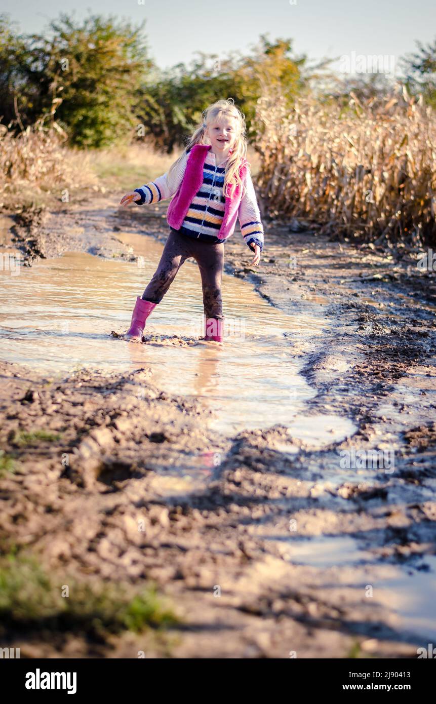 petite fille charmante qui profite d'une flaque d'eau après la pluie dans une atmosphère ensoleillée automnale saisonnière Banque D'Images