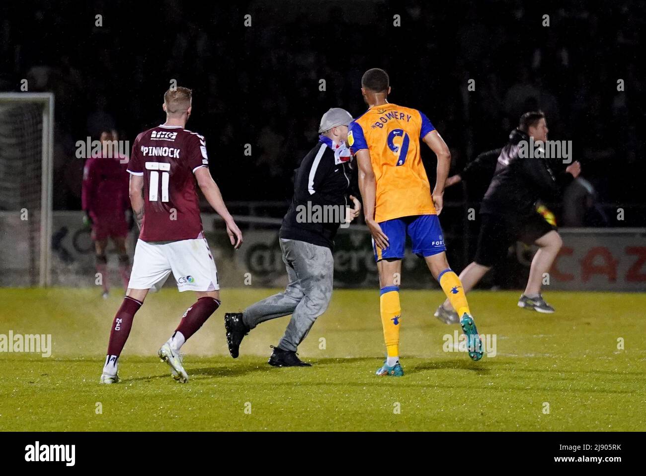 Un envahisseur de terrain (au centre) le long de la Jordan Bowery de Mansfield Town pendant la Sky Bet League deux demi-finale de match, deuxième match de jambe au Sixfields Stadium, Northampton. Les matchs de l'EFL ont été entassés mercredi soir par d'autres comportements erronés de la foule, alors qu'un envahisseur de terrain s'est enjambé dans le joueur de Mansfield Jordan Bowery pendant la deuxième partie de la ligue des deux demi-finales à Northampton. Date de la photo: Mercredi 18 mai 2022. Banque D'Images