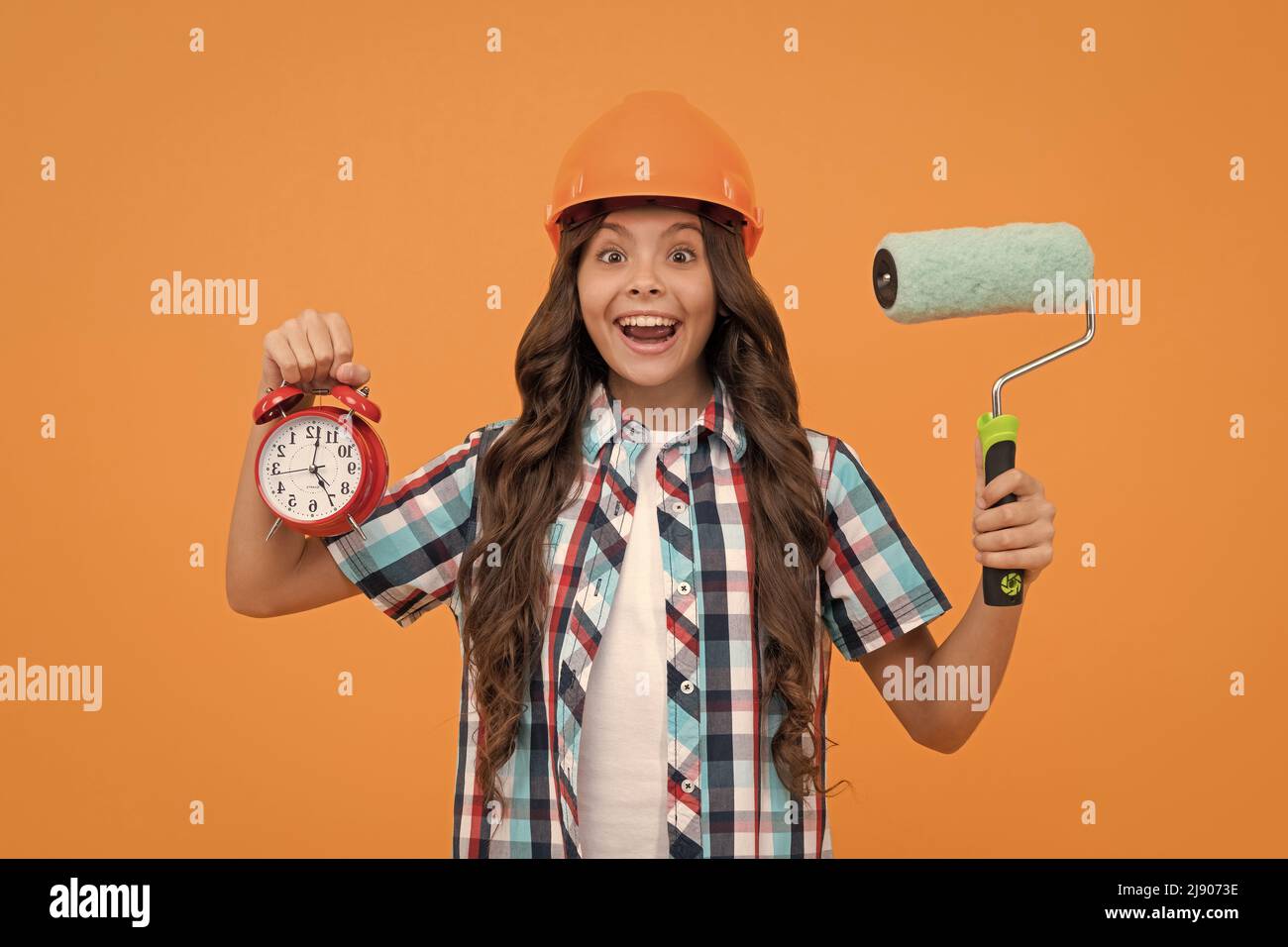 surprise adolescente tenir le rouleau de peinture et le réveil. enfant dans le casque. temps pour la décoration. Banque D'Images