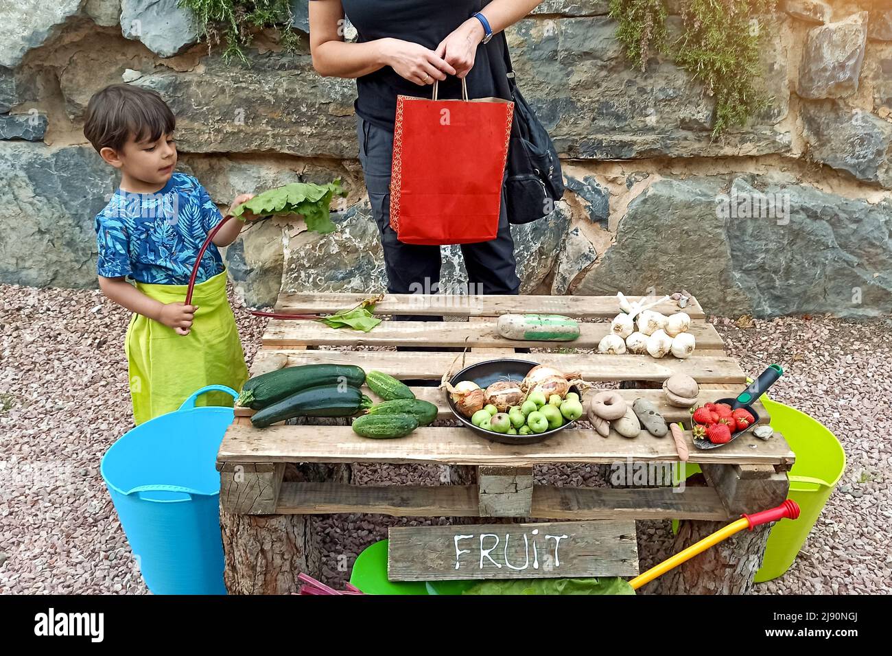 petit garçon jouant au marché des légumes avec de vrais légumes collectés dans le jardin urbain et la stalle faite avec des matériaux recyclés Banque D'Images