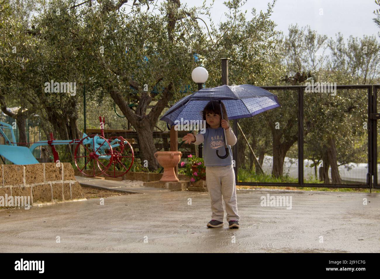 Adorable petite fille se rantant de la pluie avec un parapluie tout en jouant à l'extérieur Banque D'Images