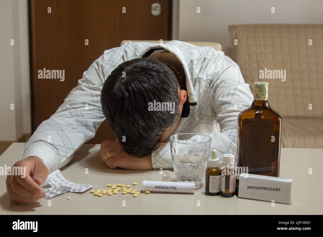 Image d'un homme dormant avec sa tête reposant sur la table après avoir consommé de l'alcool, des anxiolytiques et des antidépresseurs. Banque D'Images