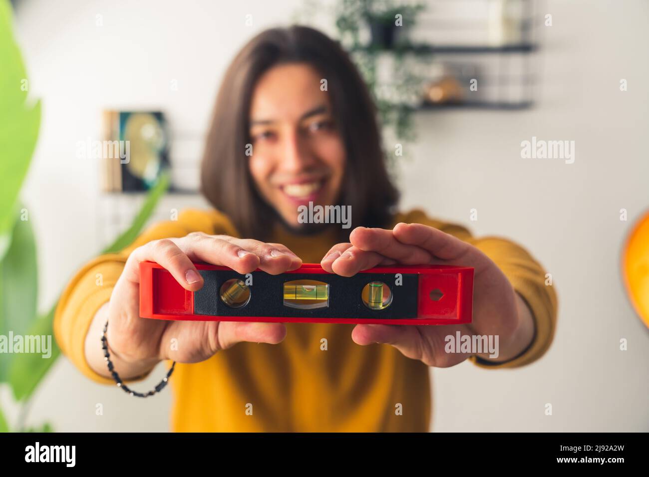 Jeune homme caucasien montre le niveau de bulle à la caméra et sourit maison rénovation concept accueil arrière-plan copie espace . Photo de haute qualité Banque D'Images