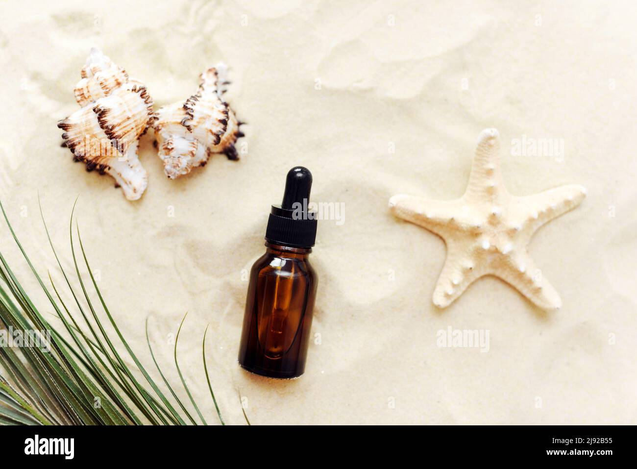Une bouteille de sérum ou d'huile, un produit cosmétique dans une bouteille en verre avec une pipette sur fond de plage avec du sable. Présentation du produit sur fond sablonneux Banque D'Images