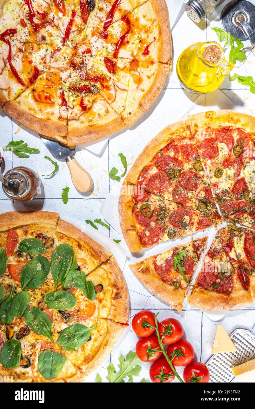 Trois pizzas variées, servies à la maison ou au restaurant sur une table carrelée avec des ingrédients de cuisine, tomate, basilic, épinards, pizza classique à l'arugula pepperoni Banque D'Images