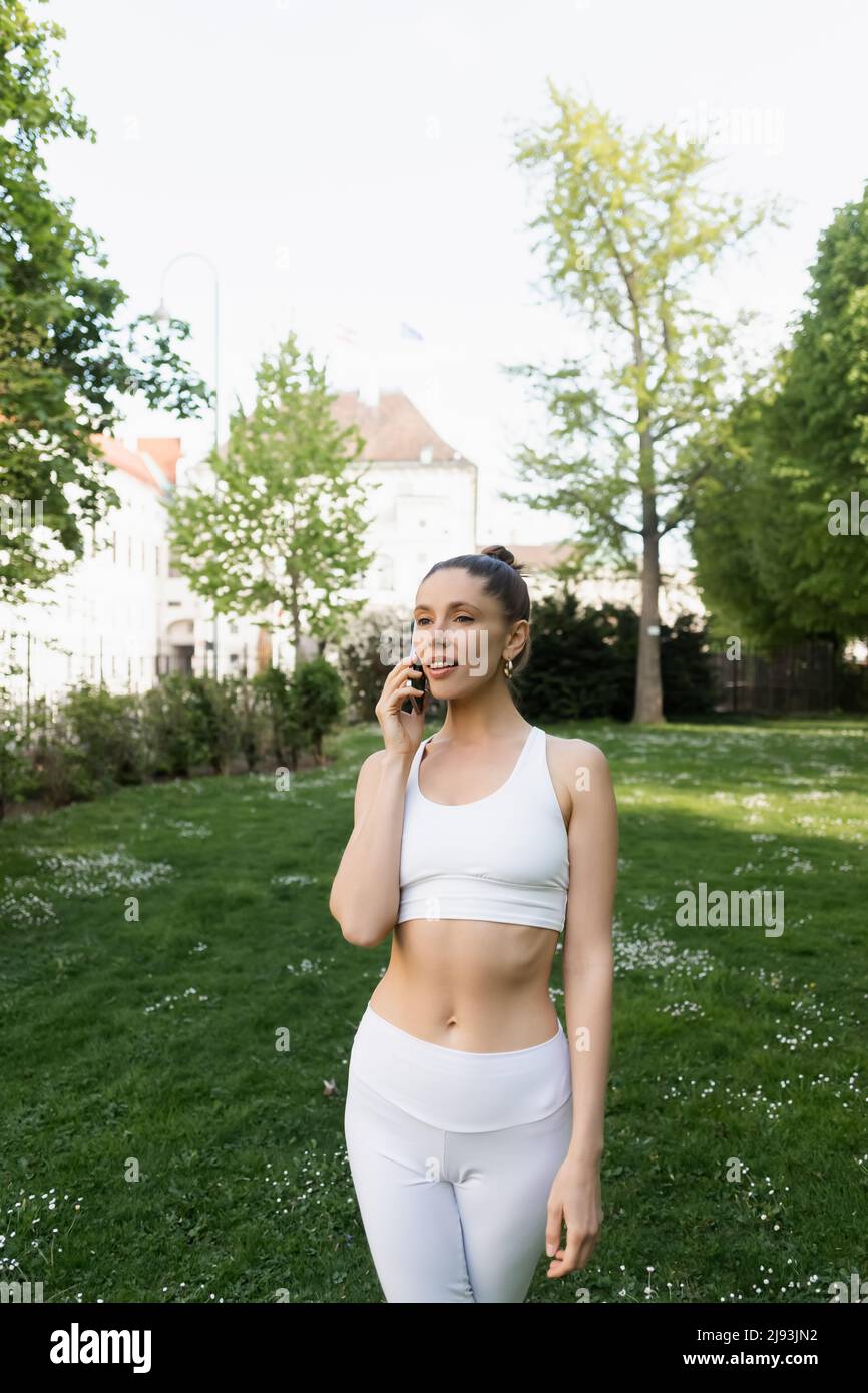 femme en soutien-gorge de sport blanc parlant sur téléphone mobile dans le parc Banque D'Images