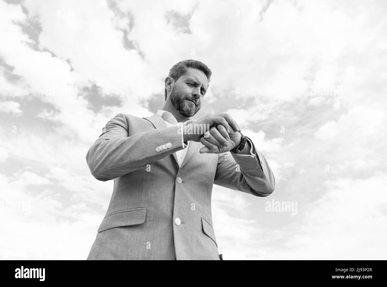 beau homme d'affaires mature dans costume formel vérifier l'heure sur montre-bracelet sur fond de ciel, échéance Banque D'Images