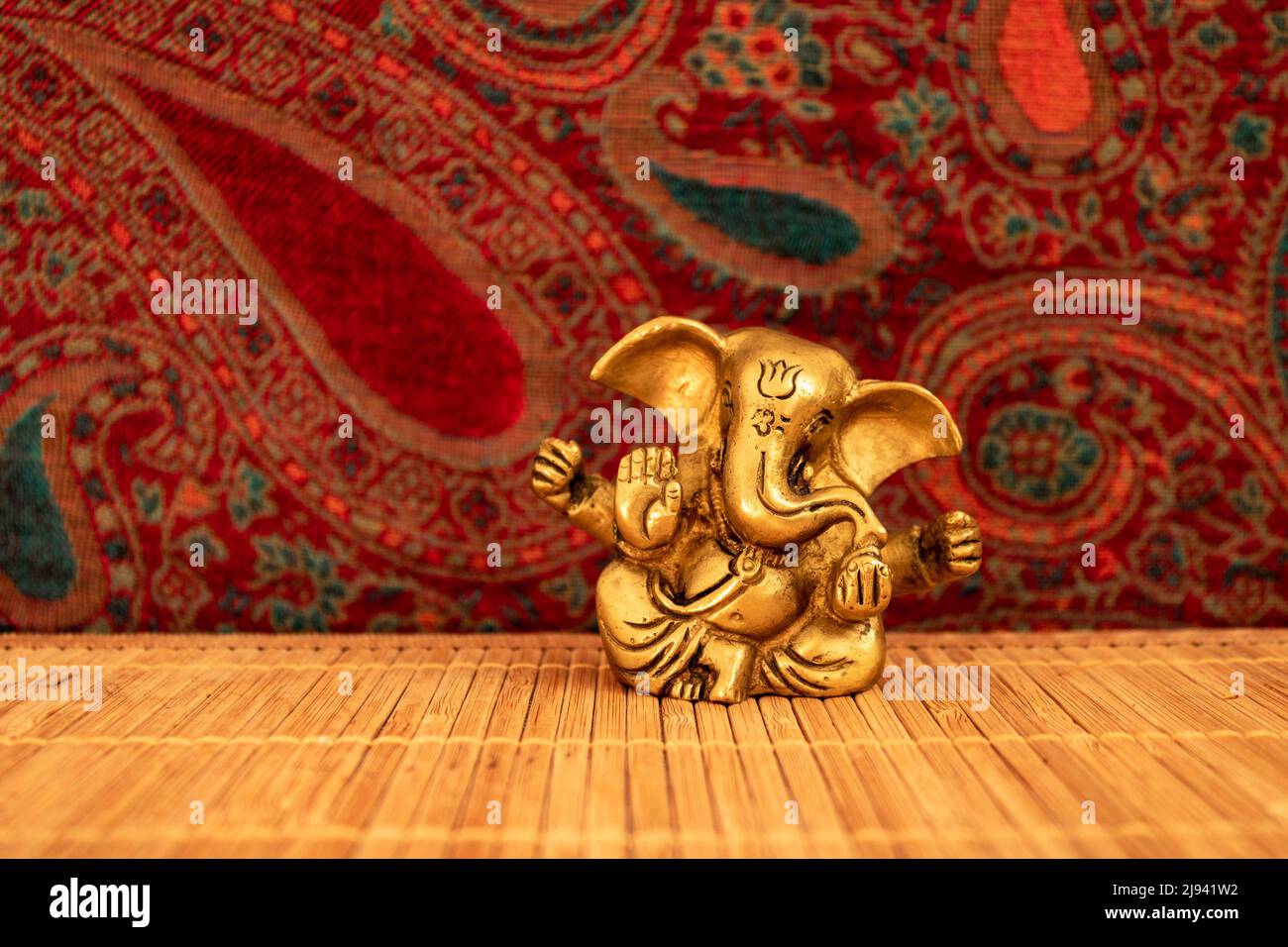 Statue de ganesha dorée sur tapis de bois avec fond coloré, gros plan. Concept de méditation et de pleine conscience Banque D'Images