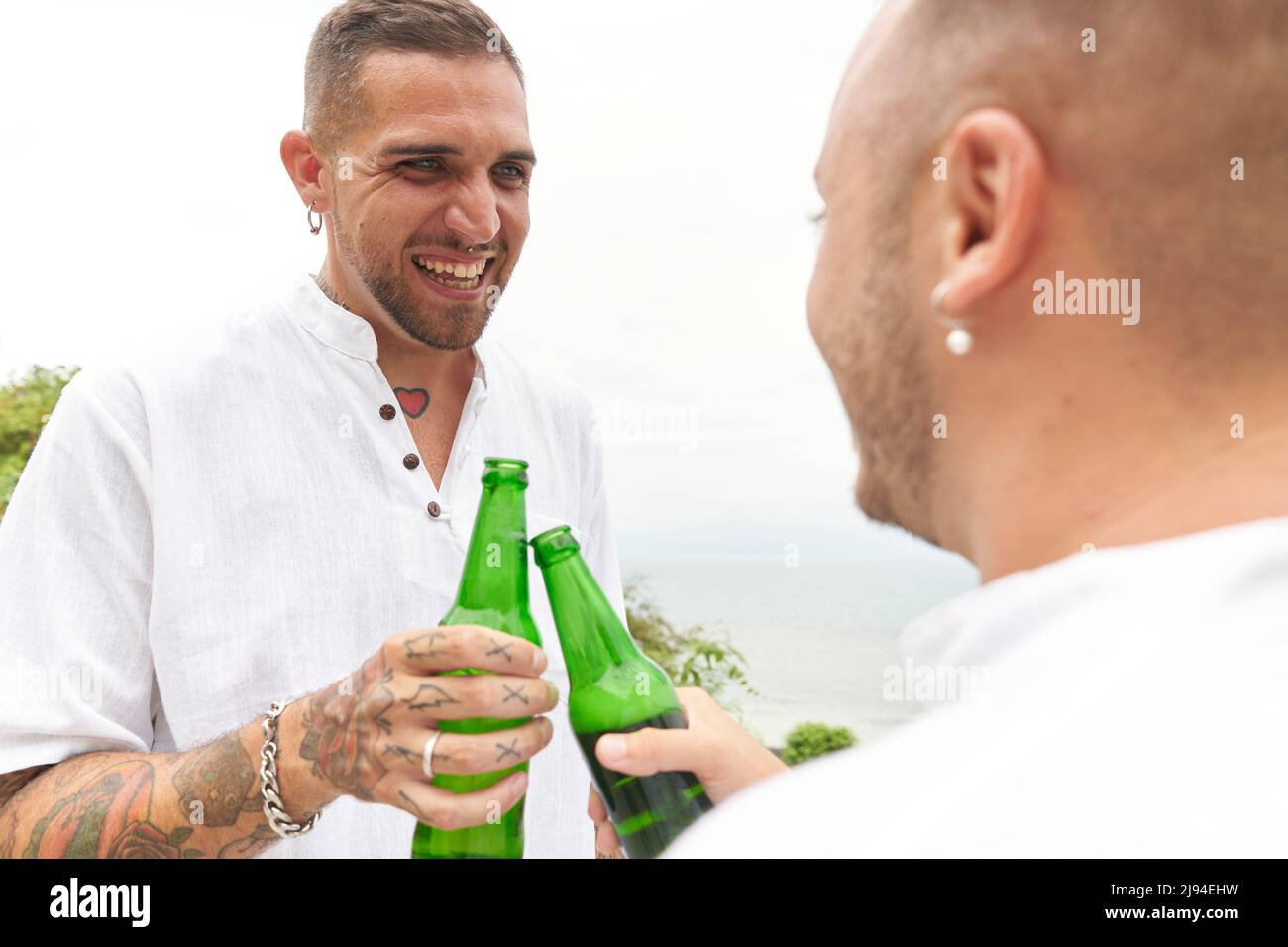 Couple gay nouvellement mariés en cours de dégustation avec de la bière au bord de la mer Banque D'Images