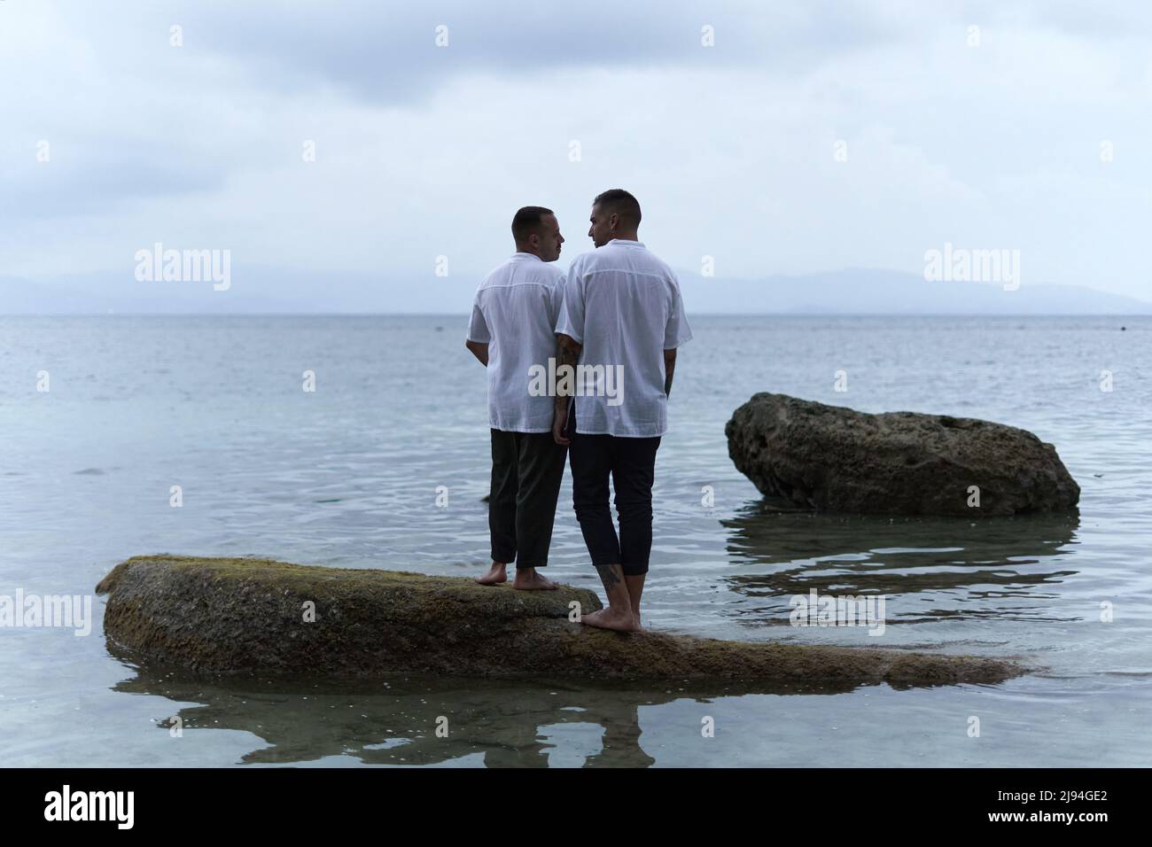 Couple gay regardant les uns les autres en faisant face à l'océan dans la soirée Banque D'Images