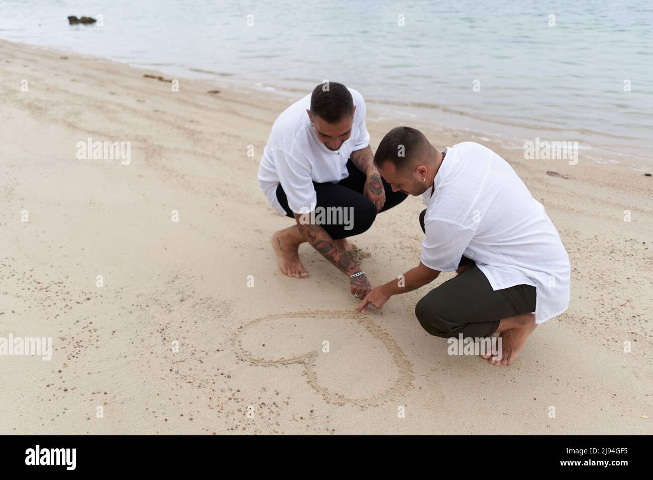 Couple gay tirant un coeur dans le sable sur une plage tropicale Banque D'Images