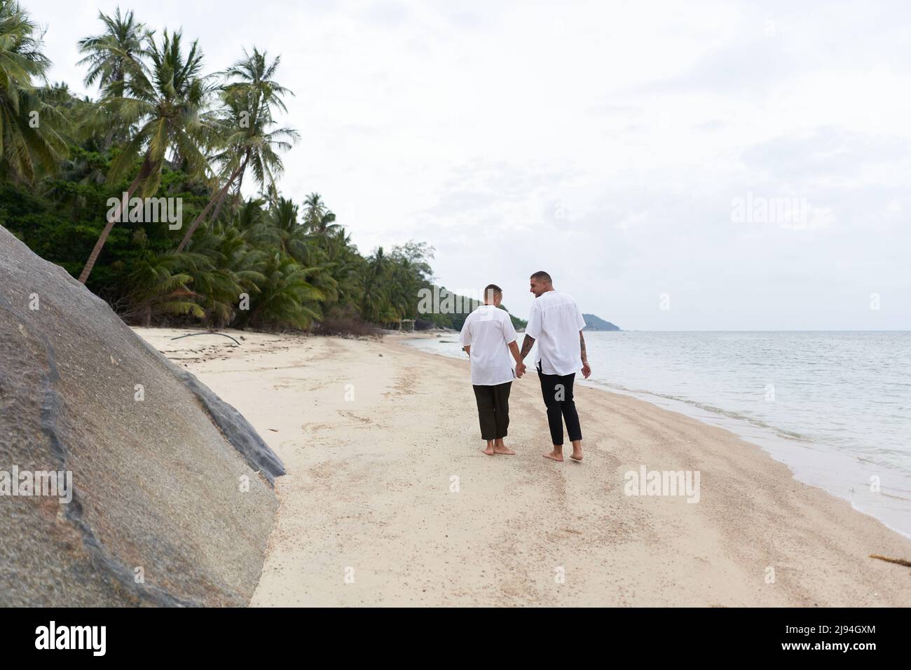 Couple gay marchant le long de la plage en tenant les mains Banque D'Images