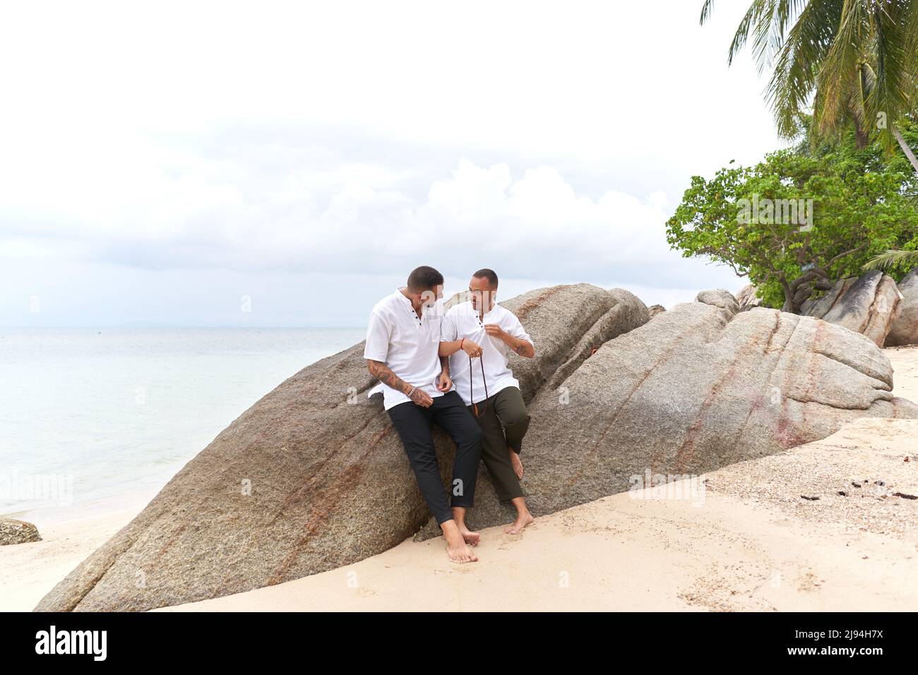 couple gay en vêtements blancs parlant sur un rocher au bord de la mer Banque D'Images