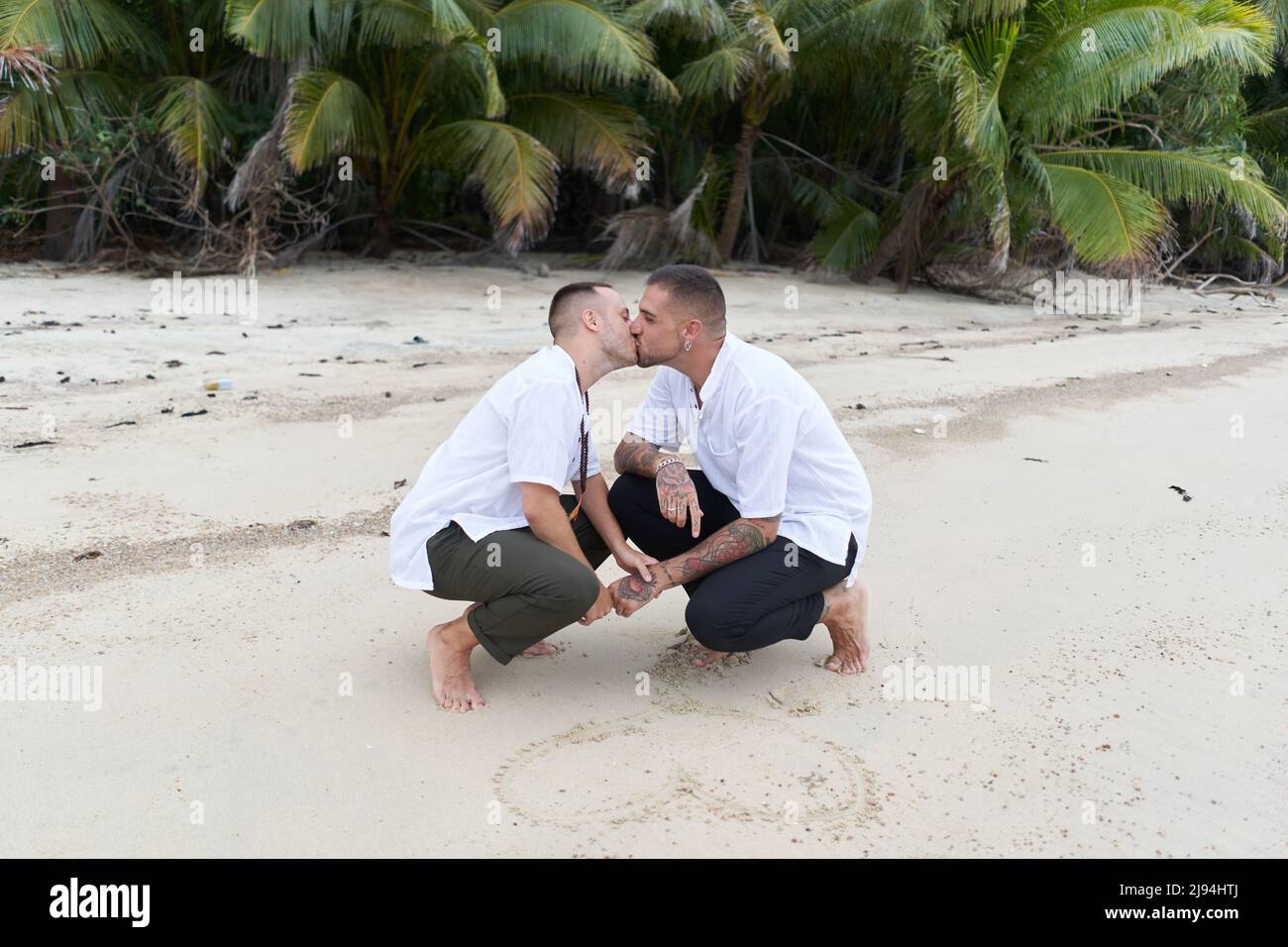Un couple gay s'accroupir sur une plage tropicale et tire un cœur dans le sable ensemble Banque D'Images