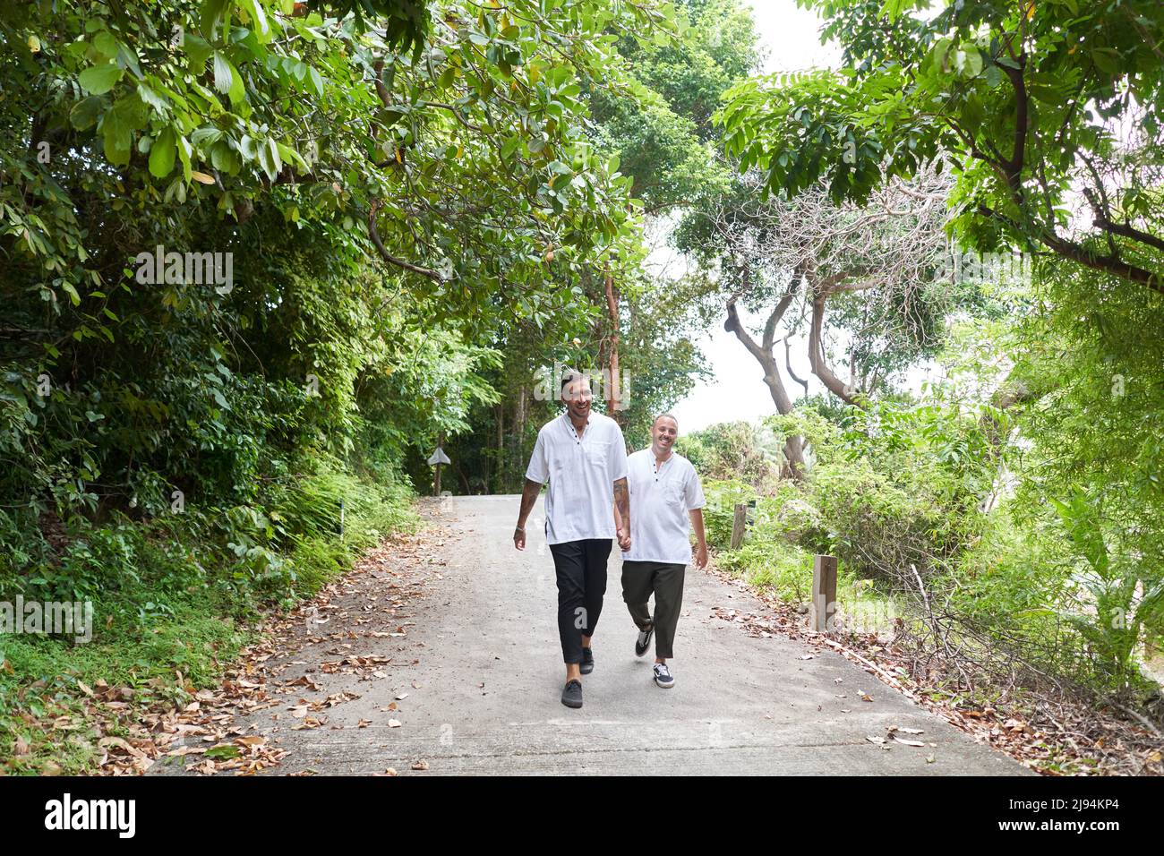 Couple gay tenant les mains tout en marchant le long d'un chemin entouré d'arbres Banque D'Images