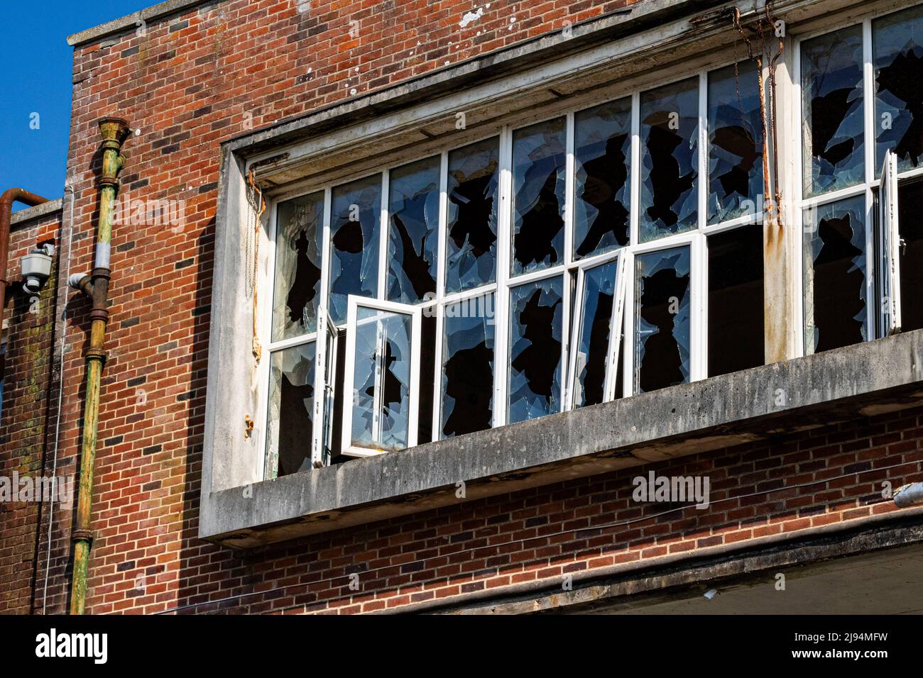 Détail des fenêtres écrasées et de l'extérieur de l'usine abandonnée Unigate contre un ciel bleu, Banque D'Images