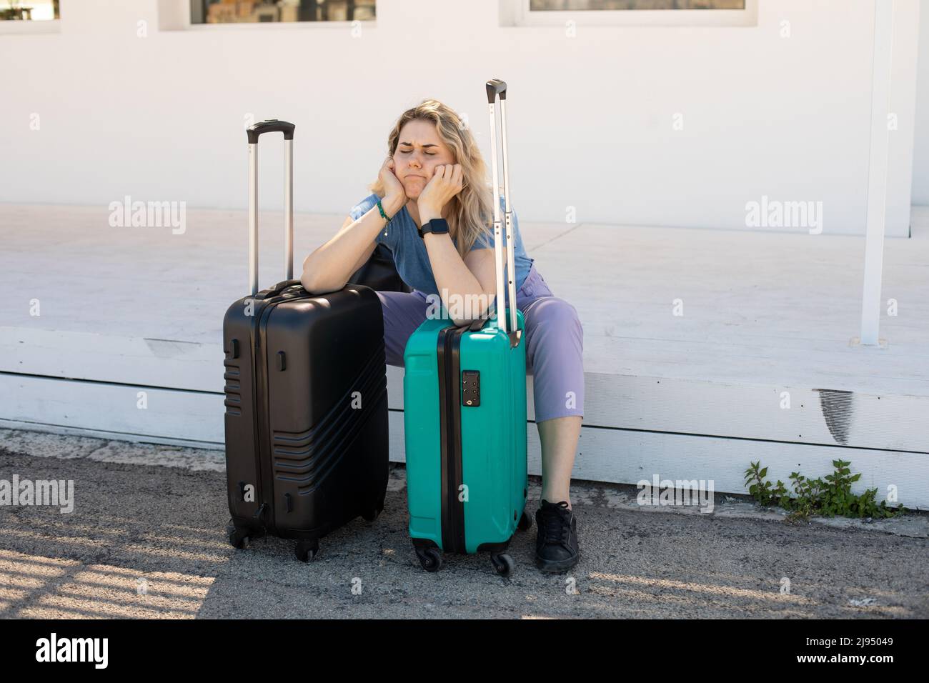 Femme blonde fatiguée, bouleversée avec des bagages, se pencher sur des sacs, assis à l'extérieur près de la gare routière sur la plate-forme, lutte de la chaleur Banque D'Images