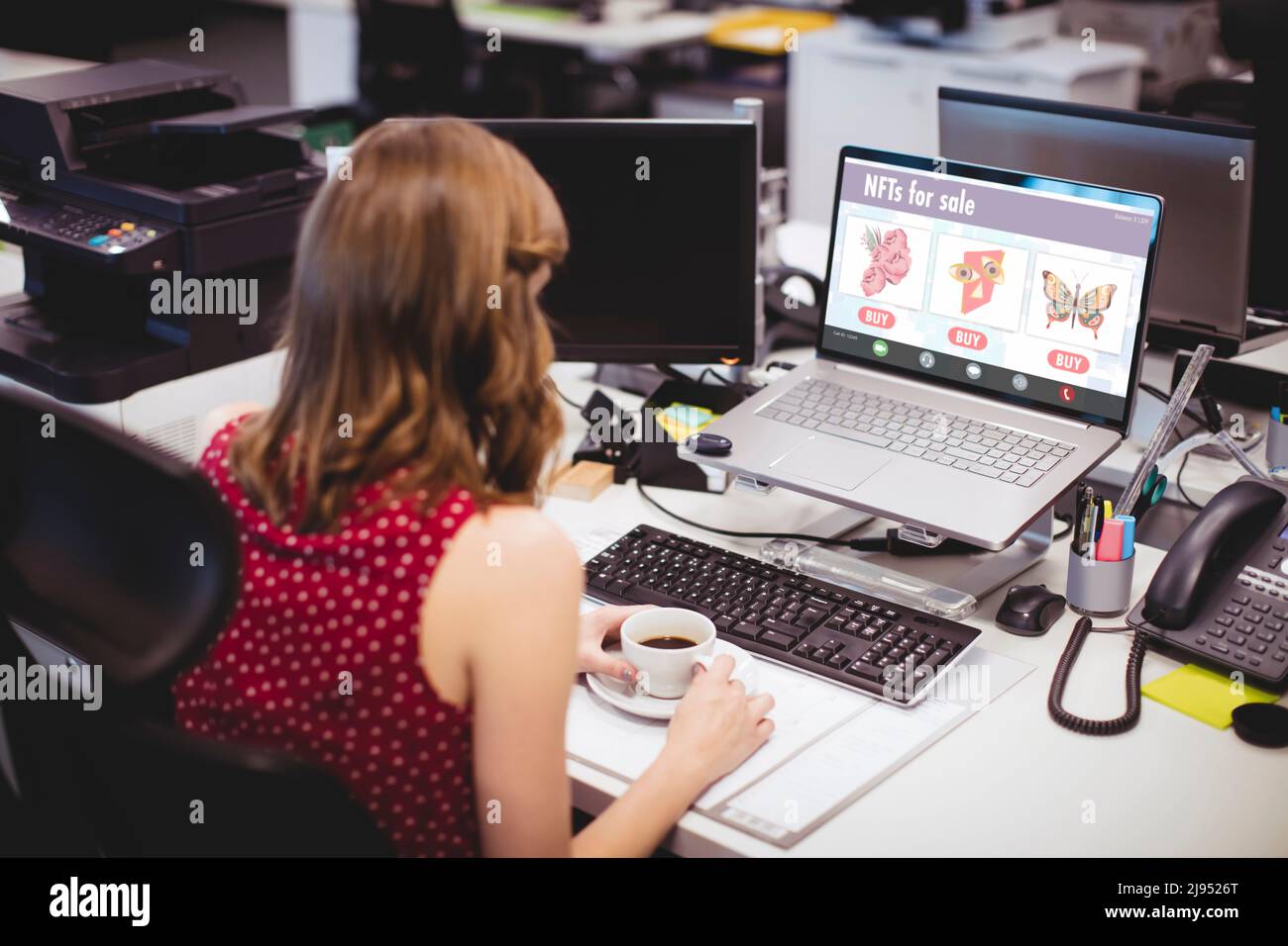 Femme d'affaires caucasienne ayant du café tout en travaillant sur des jetons non fongibles au bureau Banque D'Images