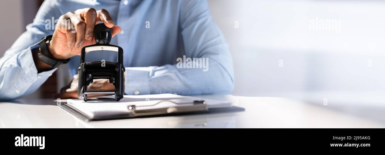 Close-up of a person's Hand Stamping avec timbre approuvé sur le document At Desk Banque D'Images