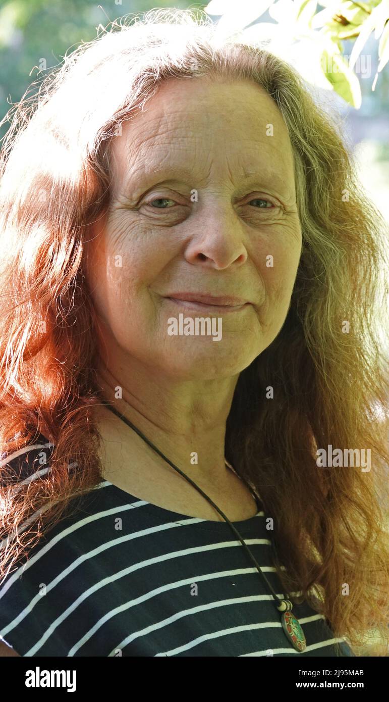 Portrait d'une femme âgée souriante sans maquillage. Ses cheveux sont de couleur mélangée : gris et rouge. Elle a des rides dans son visage et porte un SH rayé Banque D'Images