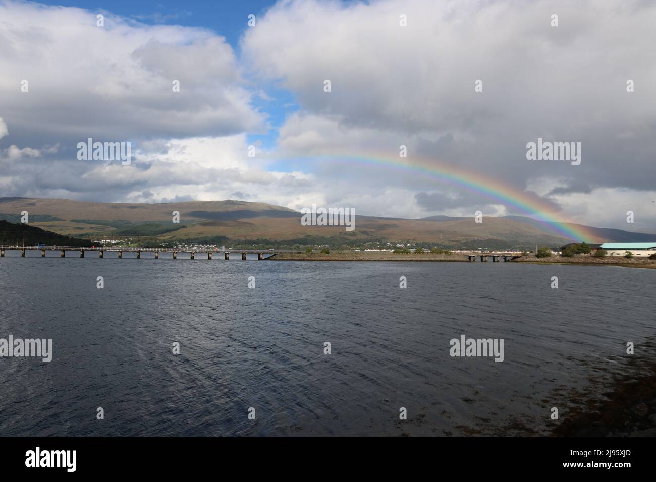 Un arc-en-ciel au-dessus d'un plan d'eau avec des nuages, un ciel bleu et des collines en arrière-plan Banque D'Images