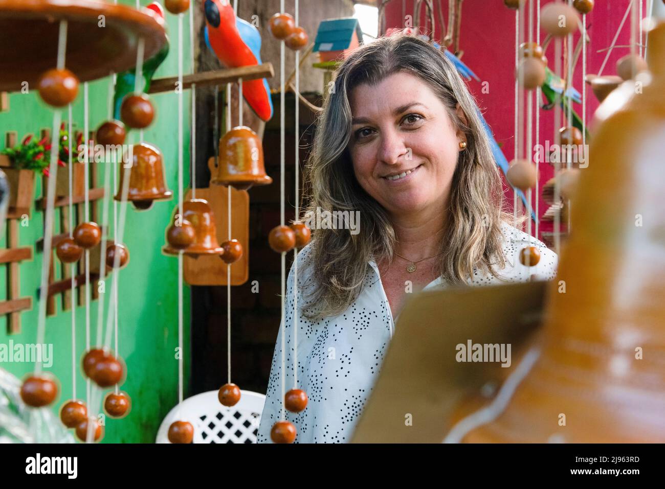 Portrait d'une femme caucasienne regardant et souriant à l'appareil photo parmi les objets décoratifs en arrière-plan. Maragogipinho, Bahia, Brésil. Banque D'Images