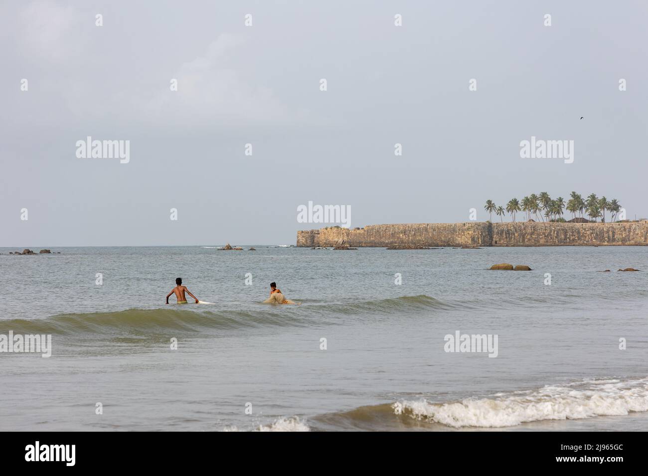 Deux pêcheurs s'aventurant dans la mer pour déposer des filets de pêche tandis que l'énorme mur en pierre du fort de Sindhudurg est vu en arrière-plan Banque D'Images